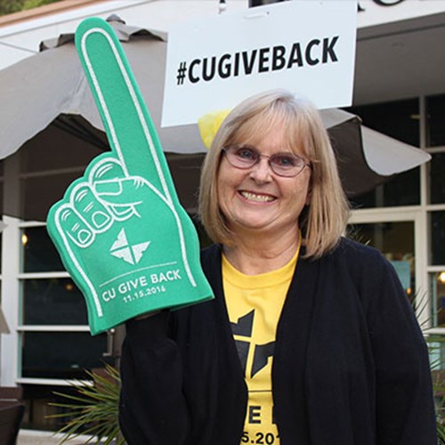 A woman stands holding a giant foam green hand with a #1 finger